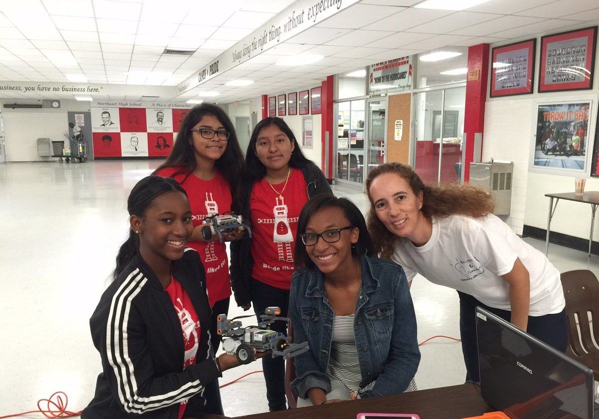 Five people pose around a robot in a hallway, smiling at a table with equipment.