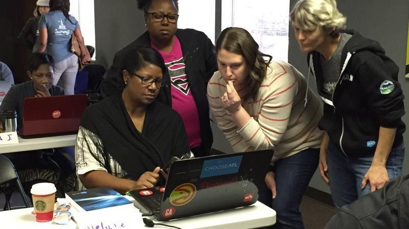 People gathered around a laptop in a meeting room, looking at the screen and discussing together.