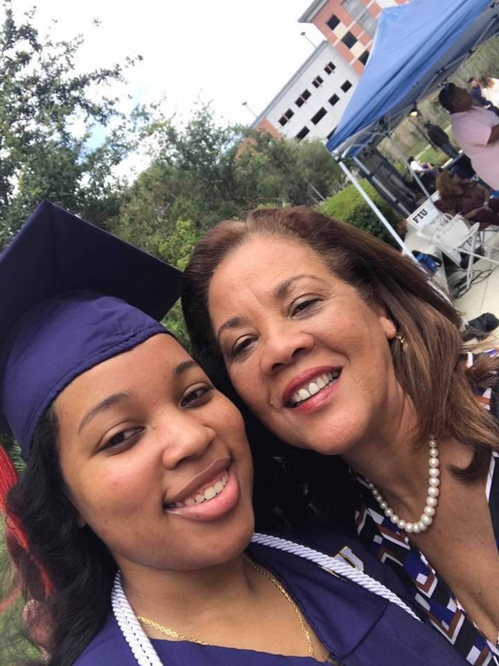 Two smiling graduates in caps and gowns posing outdoors at a commencement ceremony