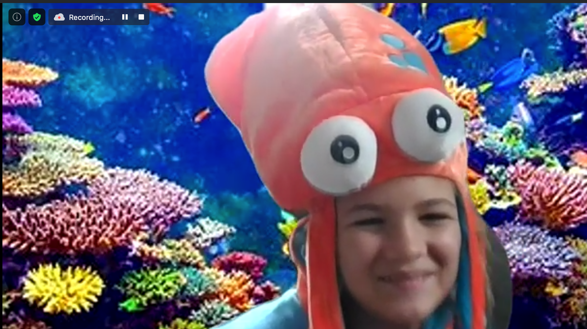 Smiling person wearing a pink octopus hat in front of a colorful coral reef backdrop