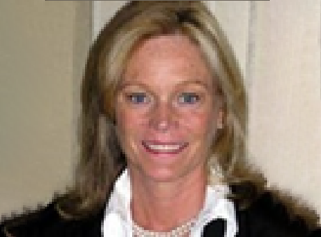 Smiling person in a black jacket and white blouse against a beige background