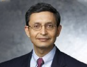 Portrait of a man in a dark suit, light shirt, and tie against a gray studio background