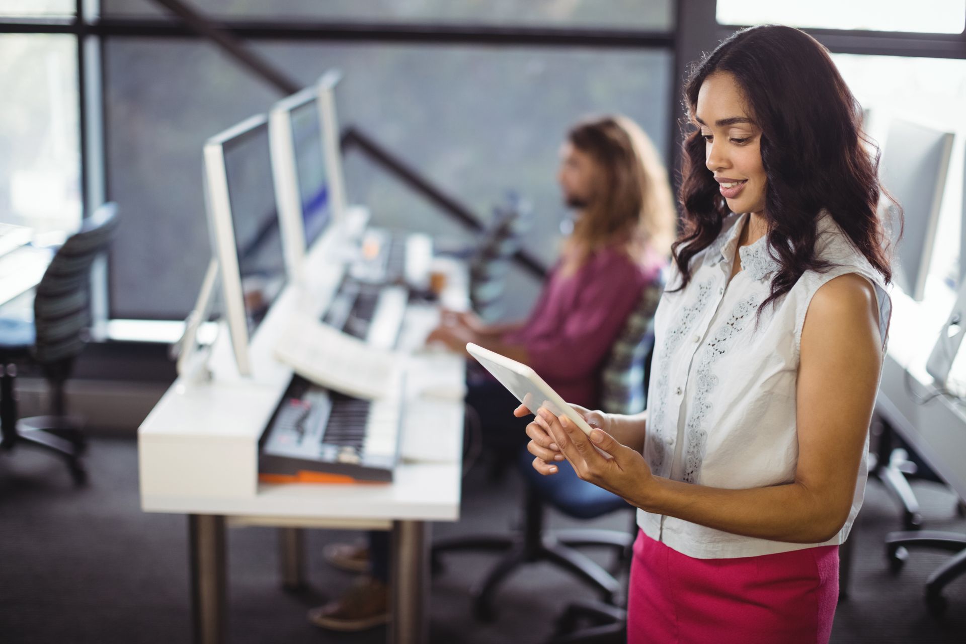Woman using a tablet in an office with coworkers at computer stations