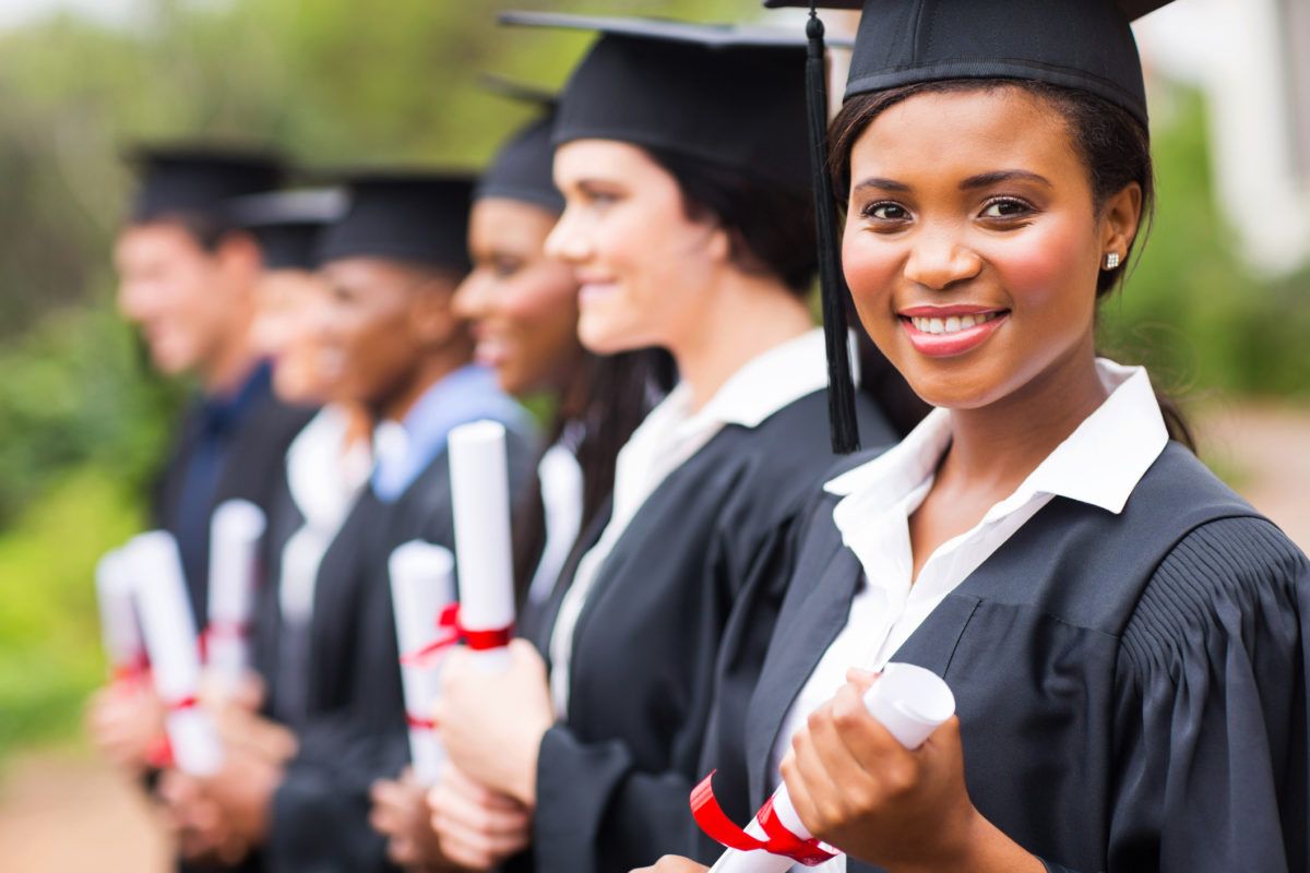 Graduates in caps and gowns holding diplomas, with one smiling in the foreground