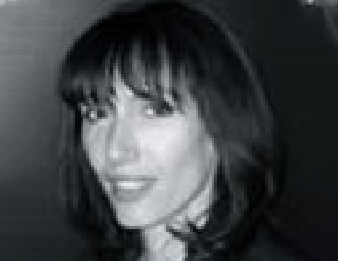 Black-and-white portrait of a smiling person with short dark hair against a dark background