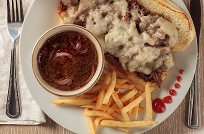 Plate with steak topped in creamy sauce, fries, red dipping sauce, and bread on a white tablecloth.