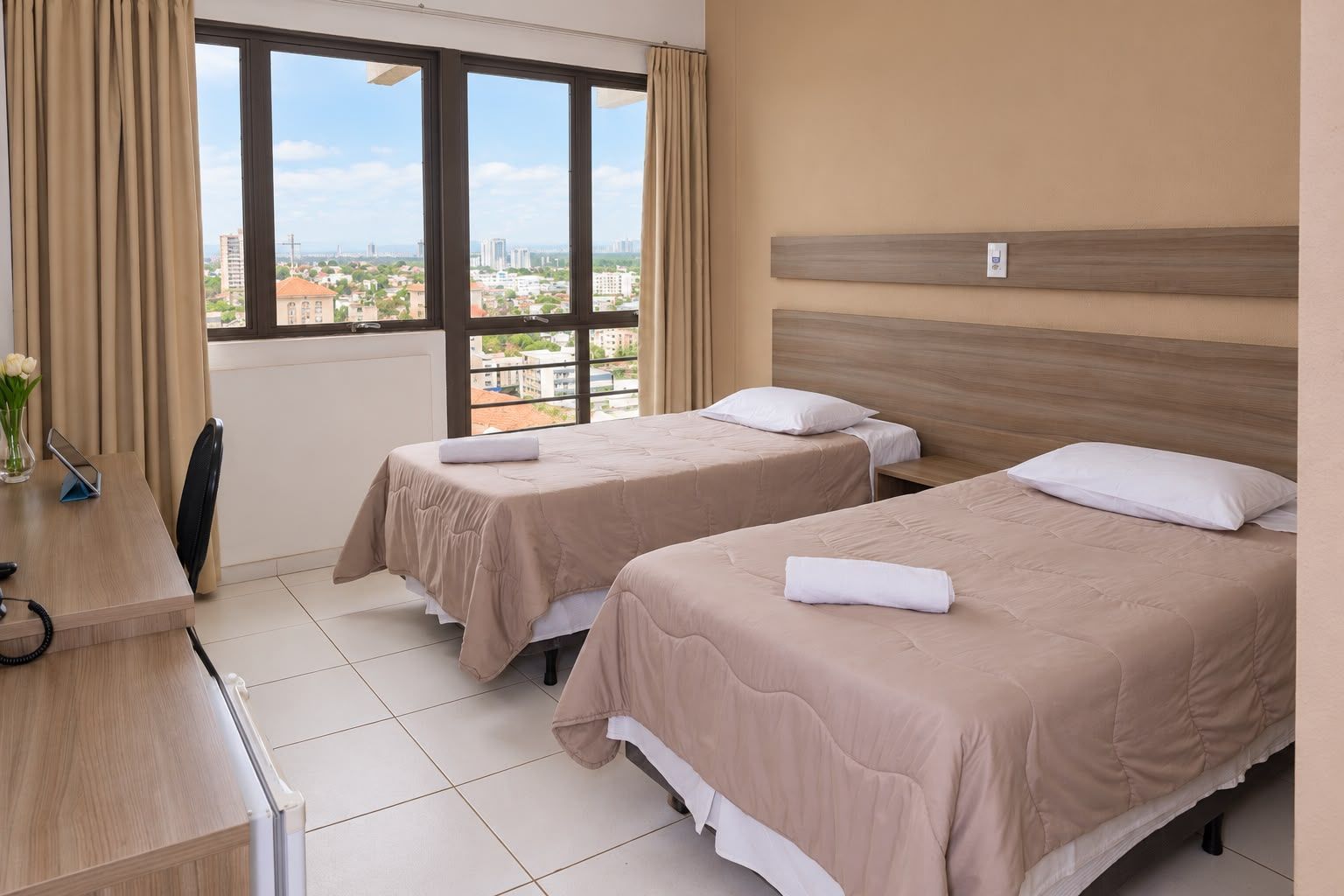 Quarto moderno com cama grande, piso de madeira, TV de parede e cortinas que vão do chão ao teto.