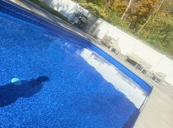 Blue swimming pool with lounge chairs and trees in the background, sunlight reflecting on the water.