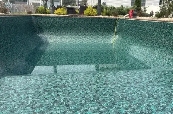 Empty mosaic-tiled swimming pool with turquoise water and a few people in the background