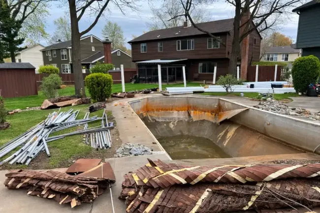 Large backyard excavation site with a deep hole, construction materials, and houses in the background