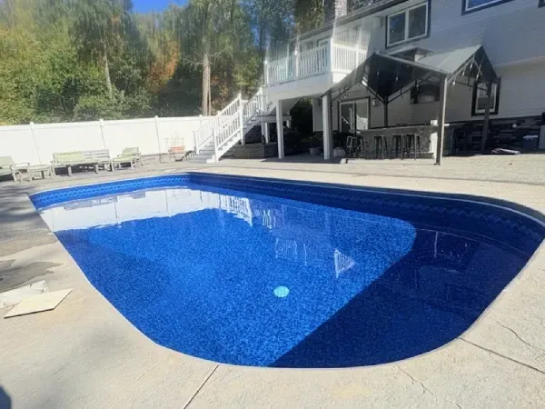 Backyard swimming pool with blue liner beside a house and patio deck