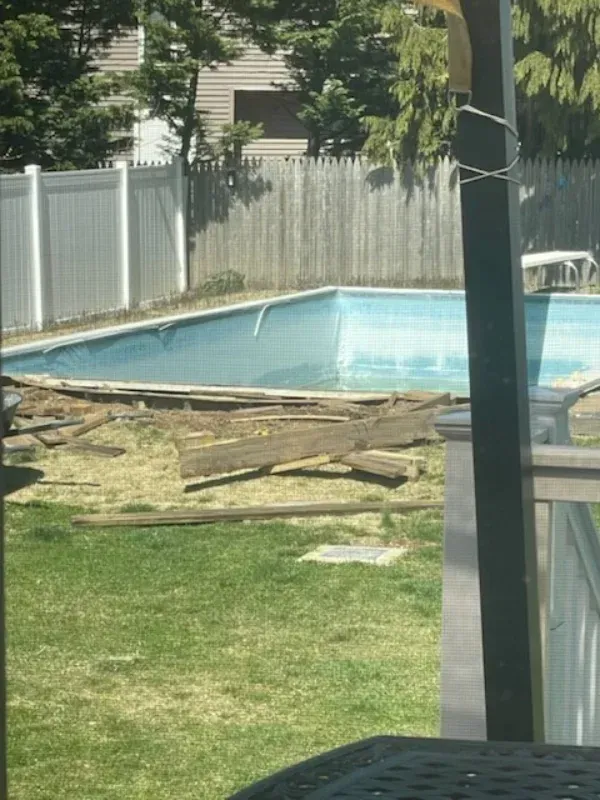 Backyard pool with scattered storm-damaged fence boards in the grass