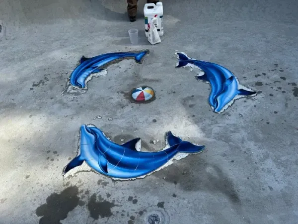 A small toy astronaut stands on concrete beside three blue inflatable dolphins around a colorful ball.