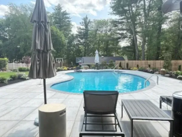 Backyard pool with blue water, lounge chairs, patio umbrella, and trees around the deck