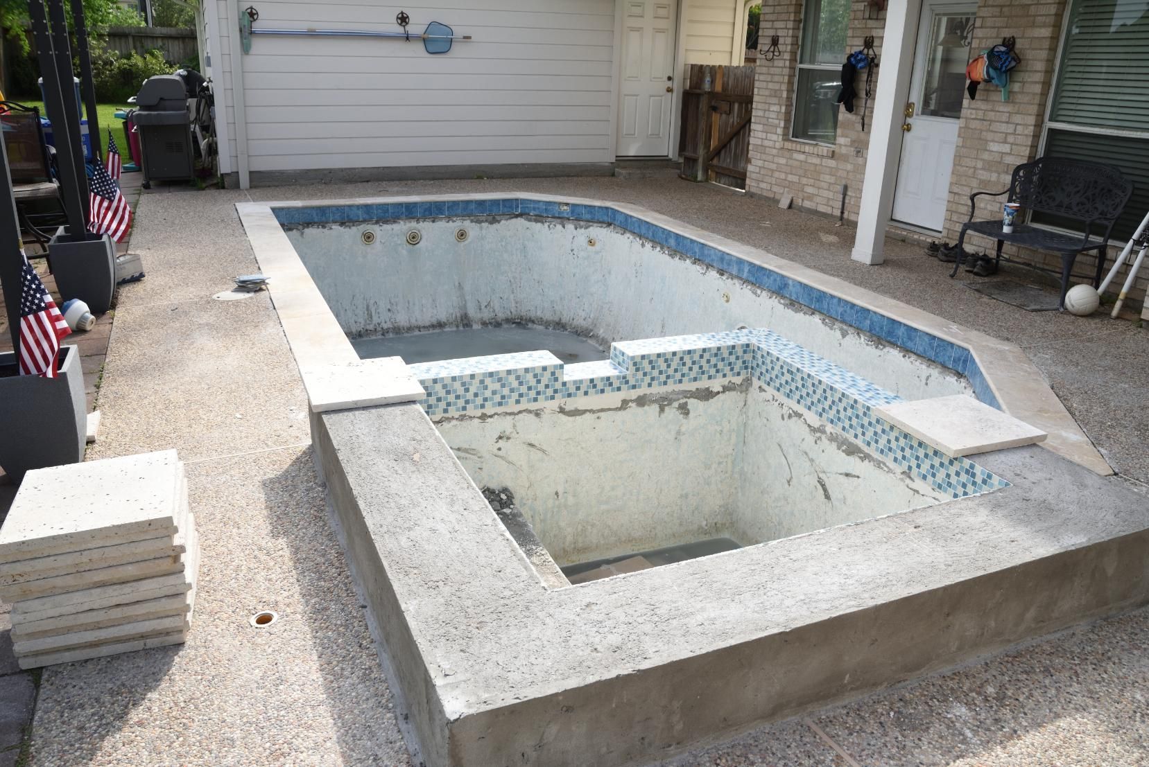 Empty backyard pool with exposed concrete and blue tile border near a garage