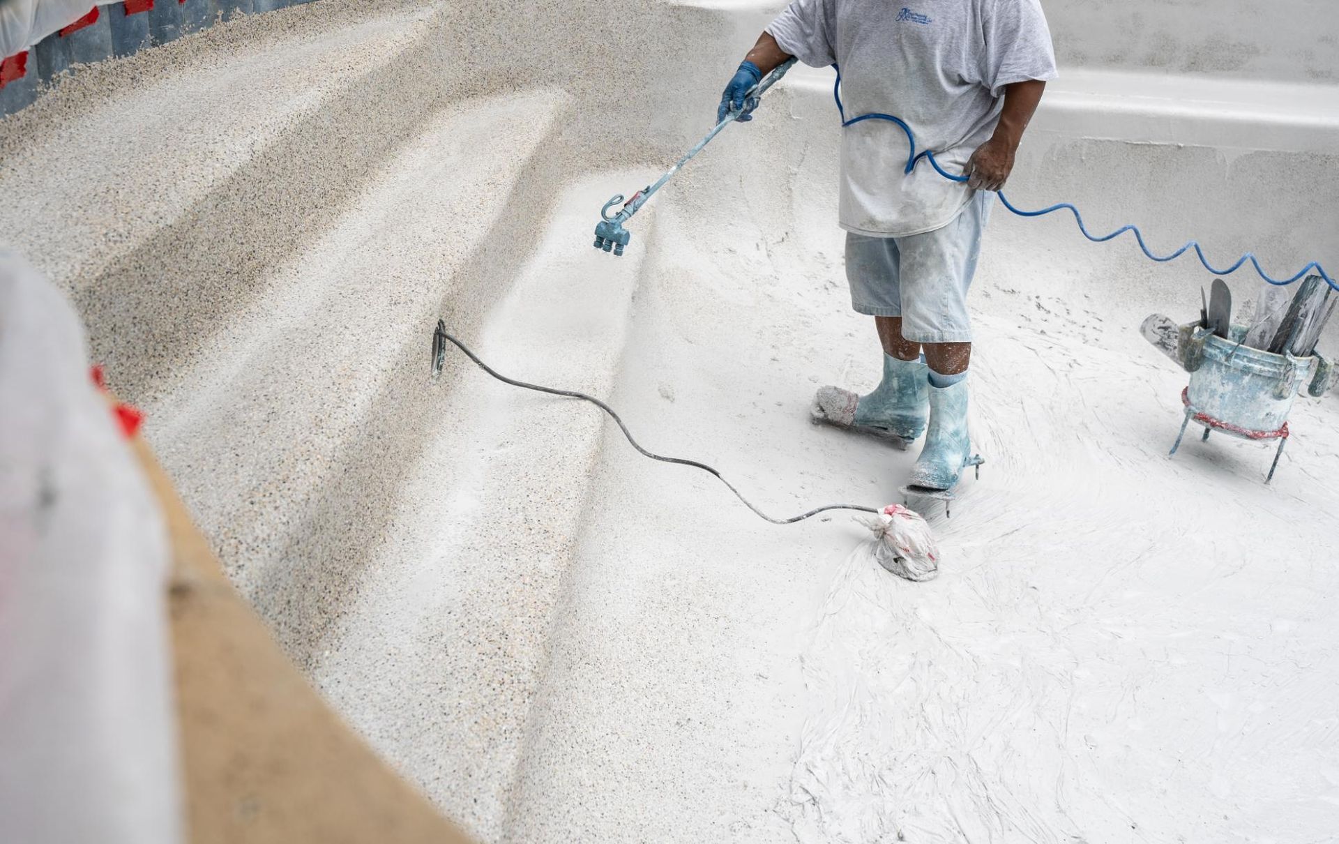Worker spray-painting a floor with a hose in a bright, mostly white room