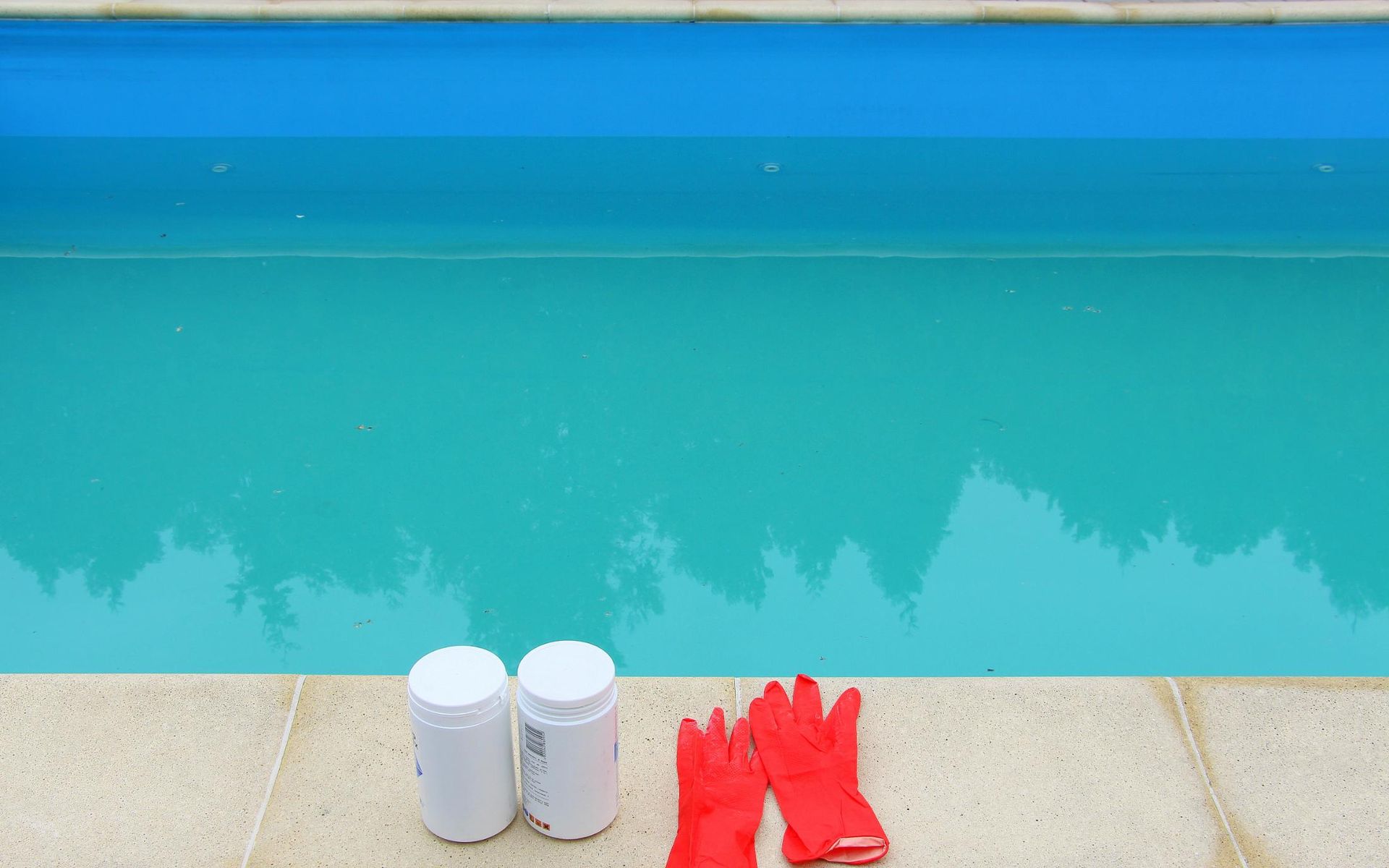 Swimming pool edge with two white bottles and a pair of red gloves on the deck