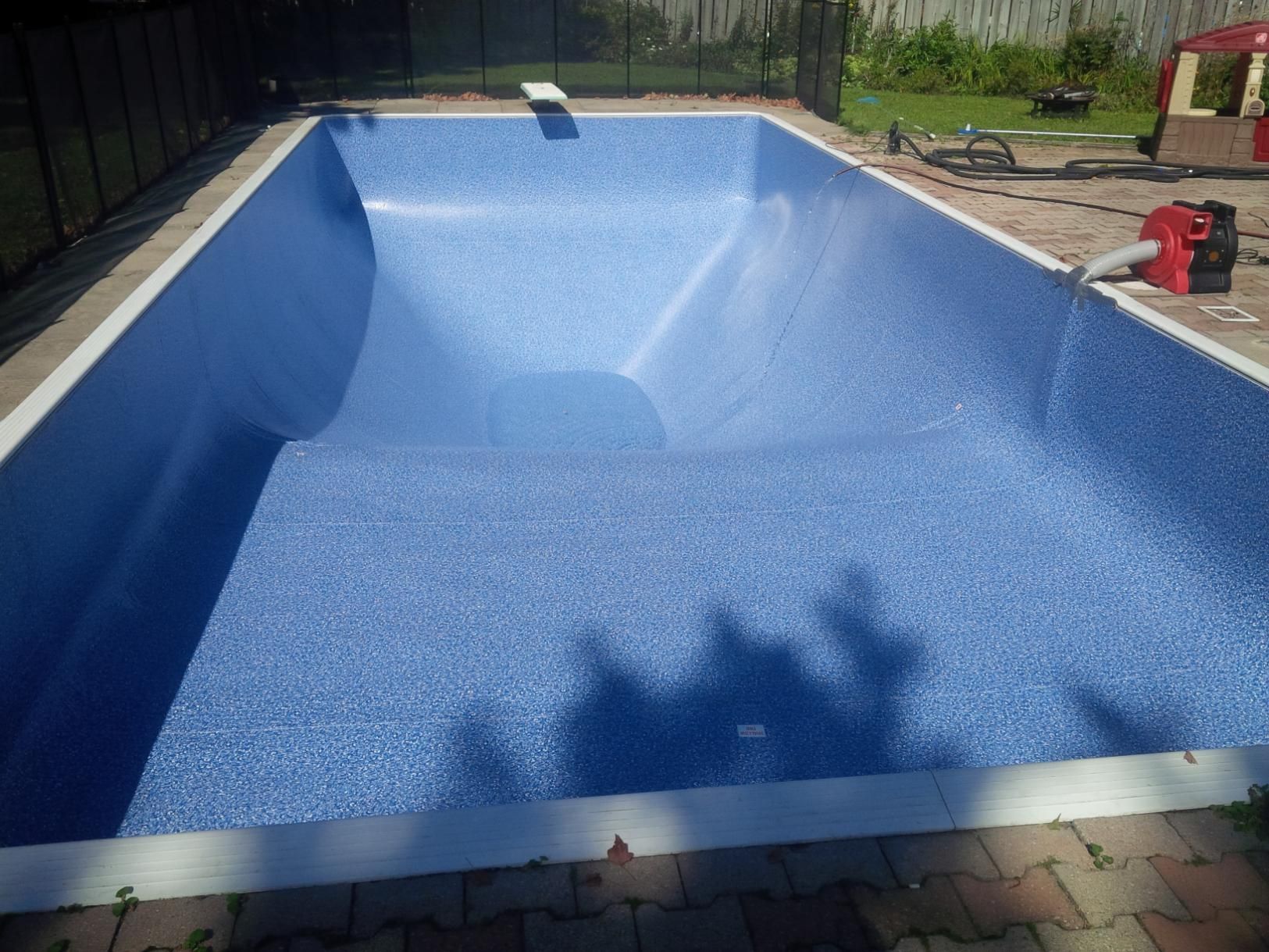 Empty blue swimming pool under construction, with surrounding fence and paving.