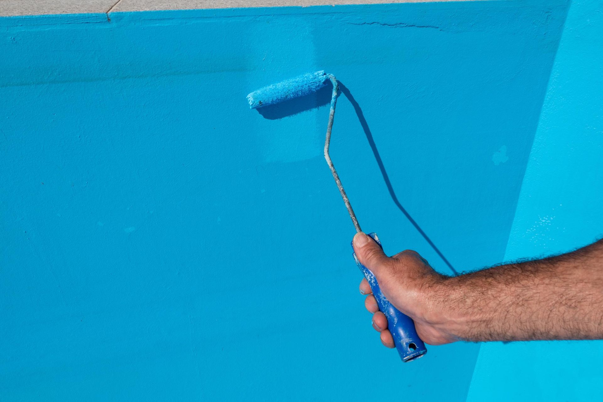 Hand using a paint roller to apply blue paint to a wall