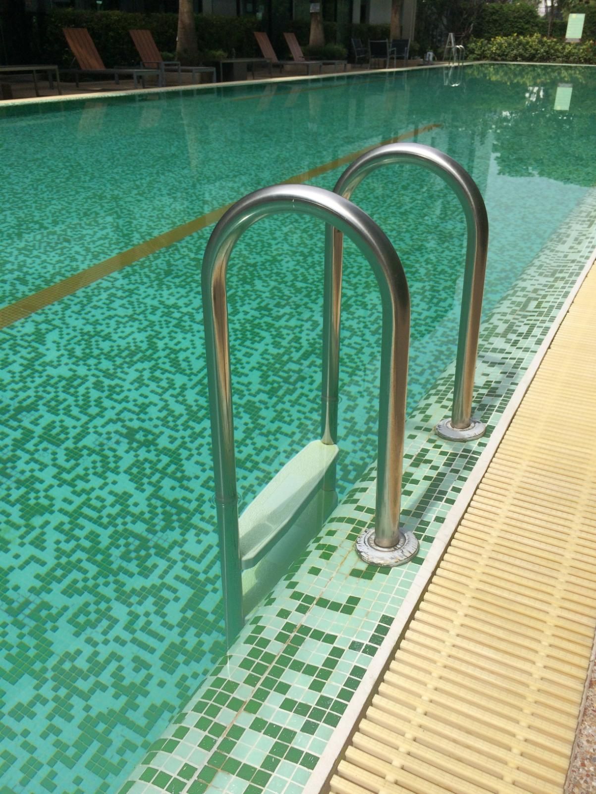 Pool ladder on the edge of a turquoise swimming pool with tiled deck and water.