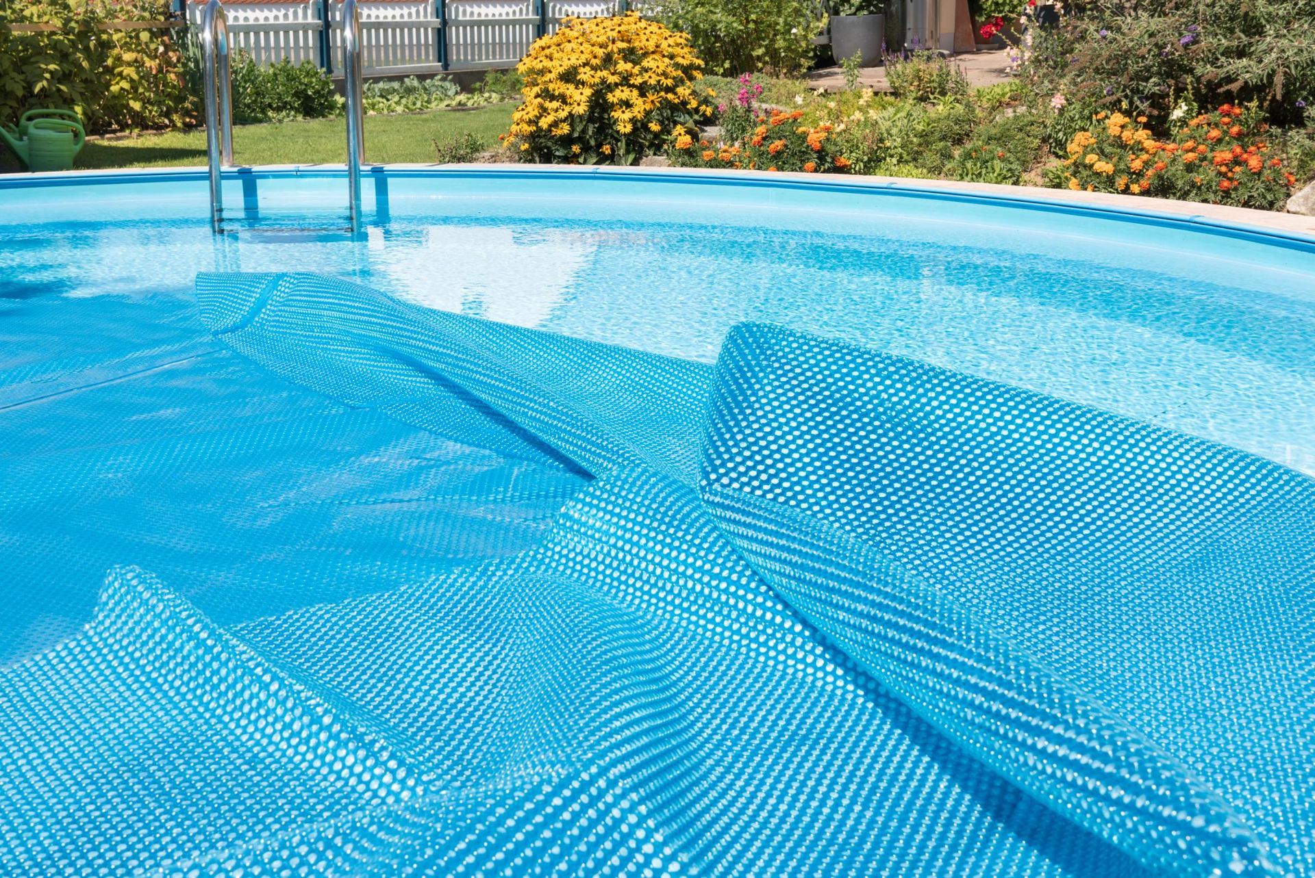 Covered blue swimming pool in a backyard with flowers and a fence in the background