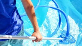 Person using a pool vacuum hose in bright blue water
