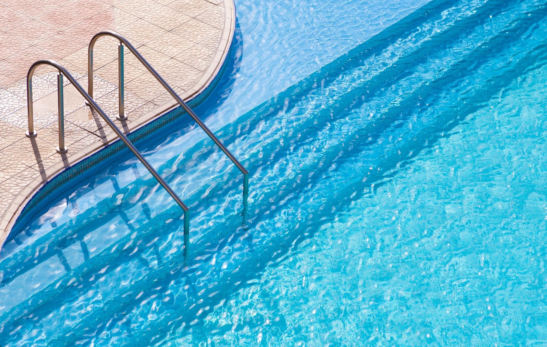 Swimming pool ladder beside bright blue water and tan pool deck
