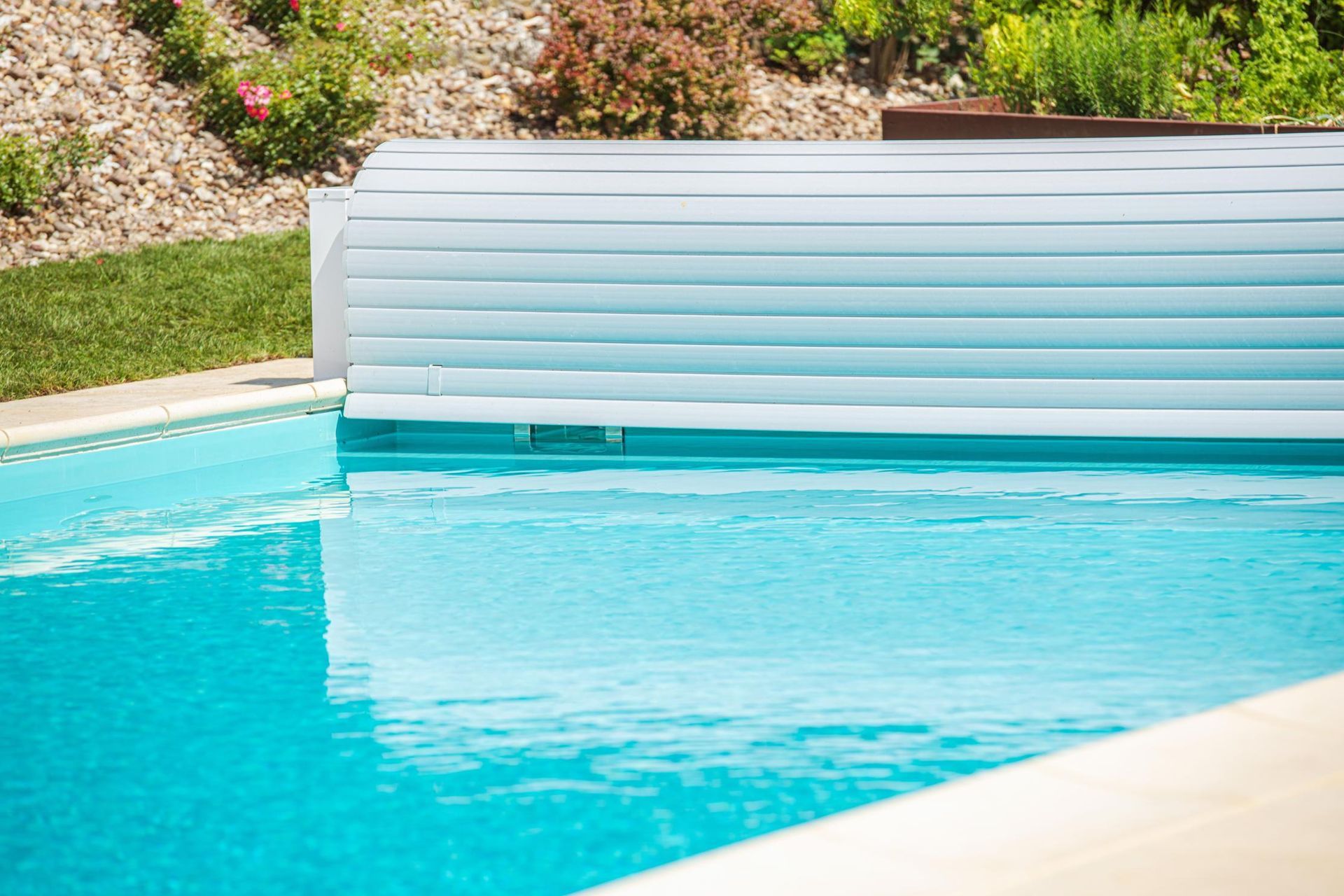Bright turquoise swimming pool with a white pool cover and stone edging