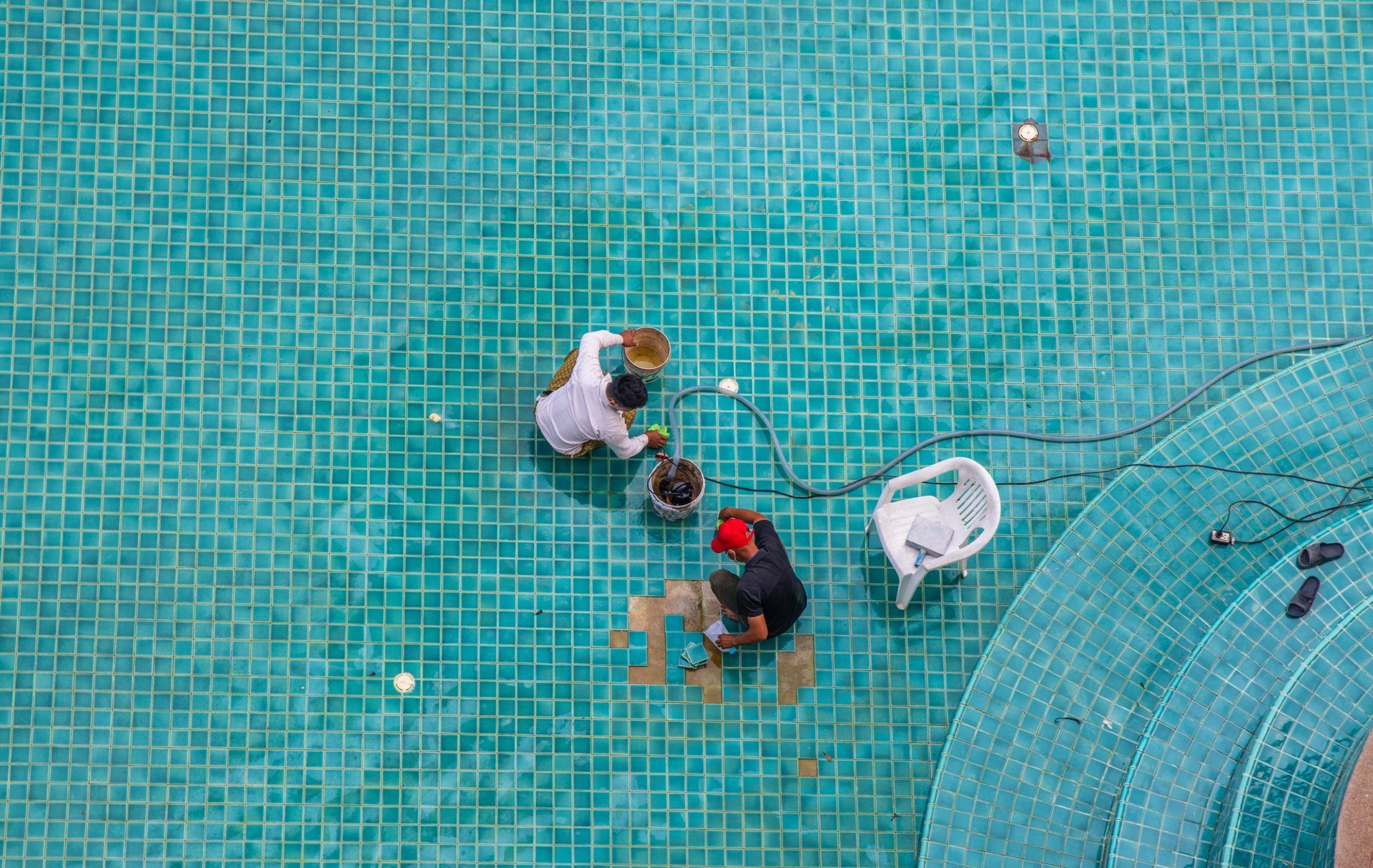 Three people with a white dog on a turquoise tiled pool deck, viewed from above