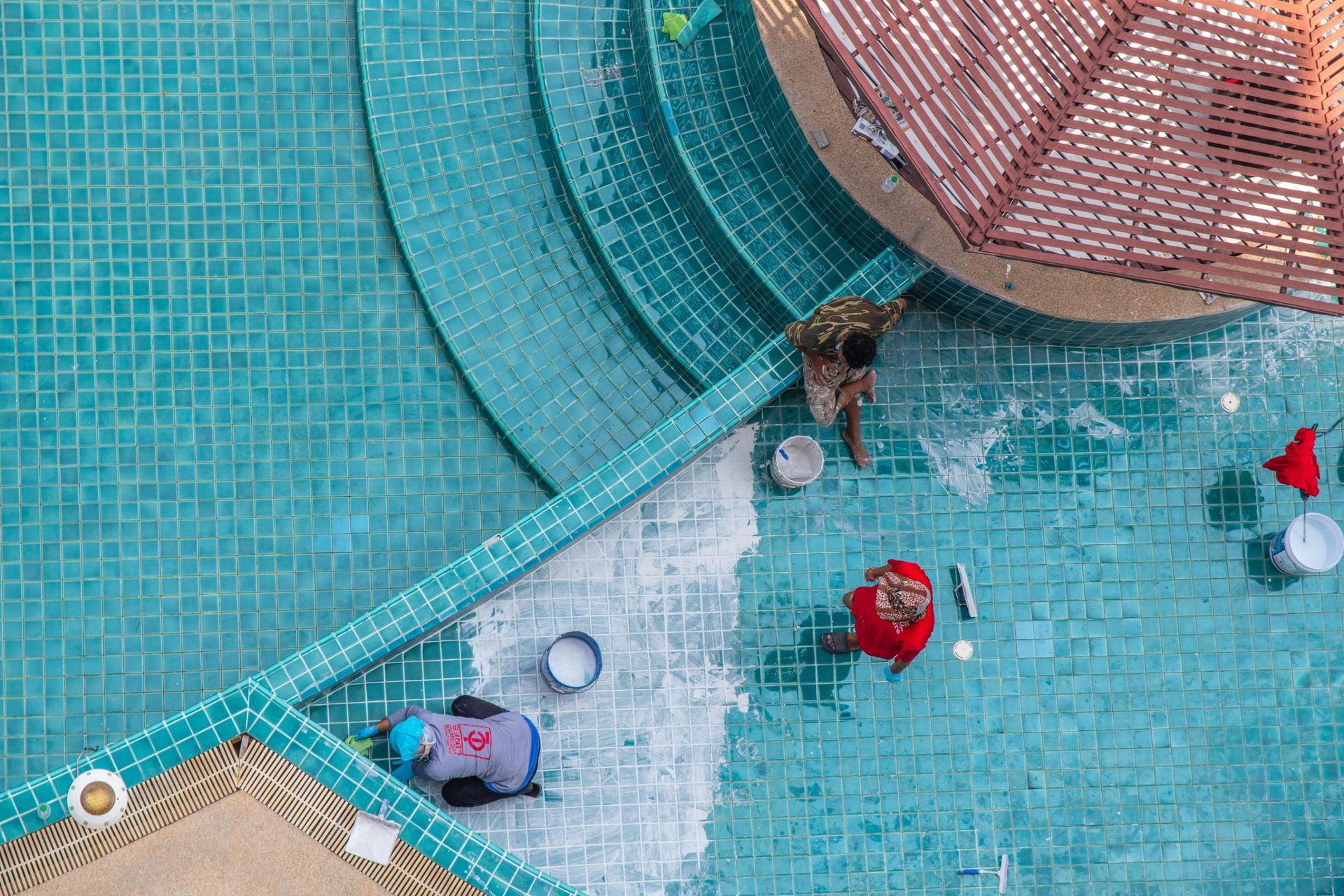 People walking in a turquoise-tiled pool with curved steps and a netted play area.