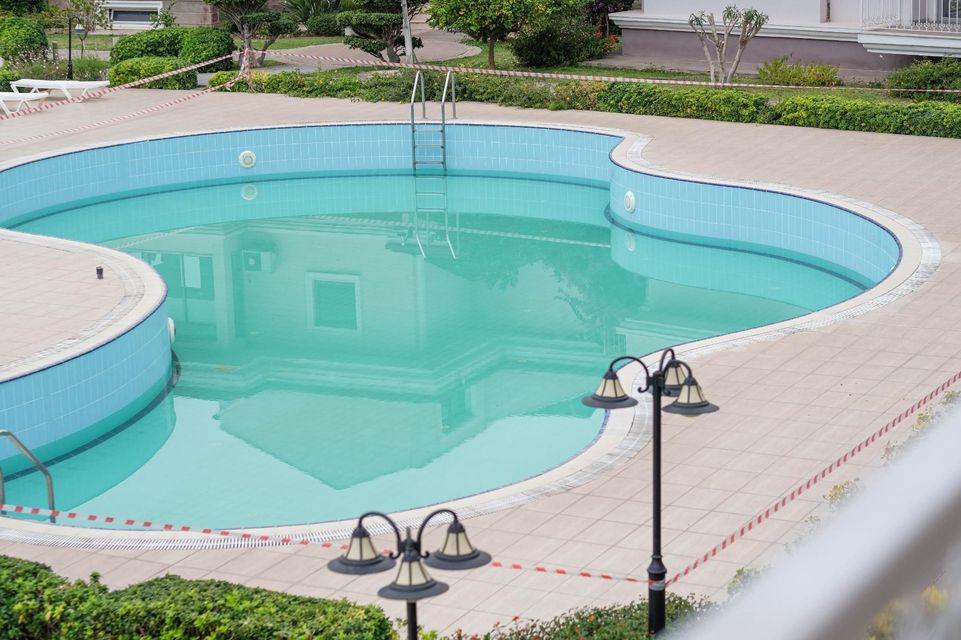 Empty turquoise swimming pool with a beige deck and black lamps in a courtyard area