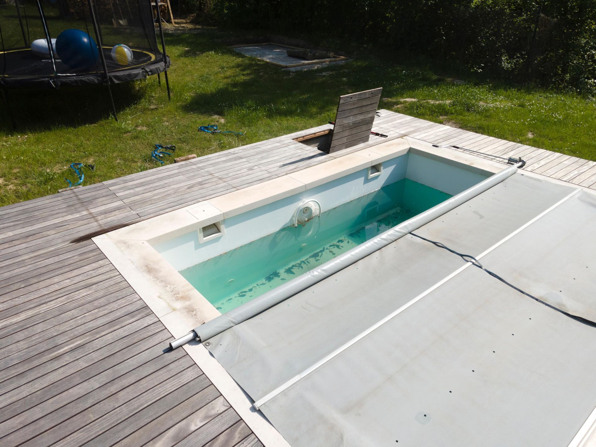 Backyard swimming pool with a white cover partly rolled back, revealing turquoise water and a deck