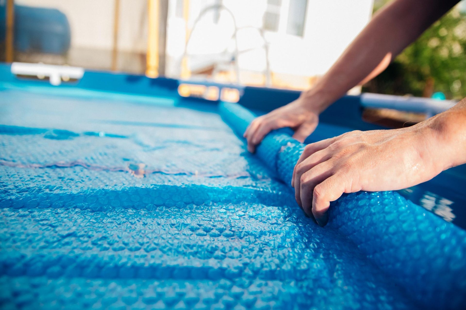 Hands rolling up a blue pool cover by a swimming pool
