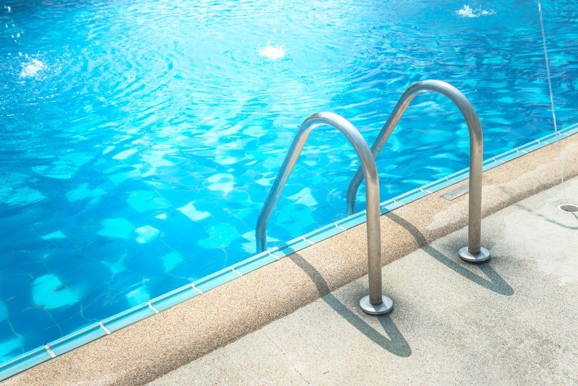 Swimming pool ladder beside clear blue water and a tiled deck