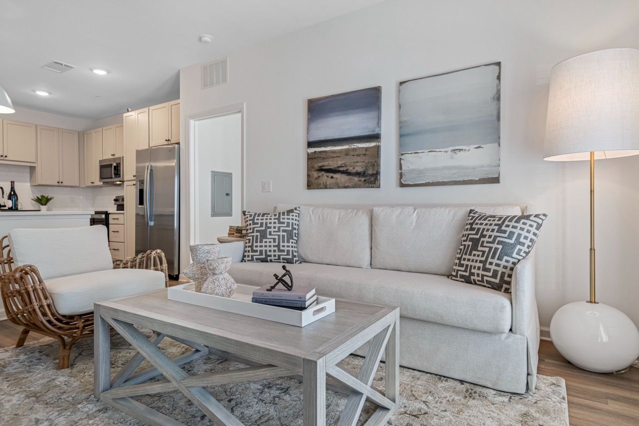 Living room in a modern apartment with a light sofa, coffee table, and open kitchen in the background.