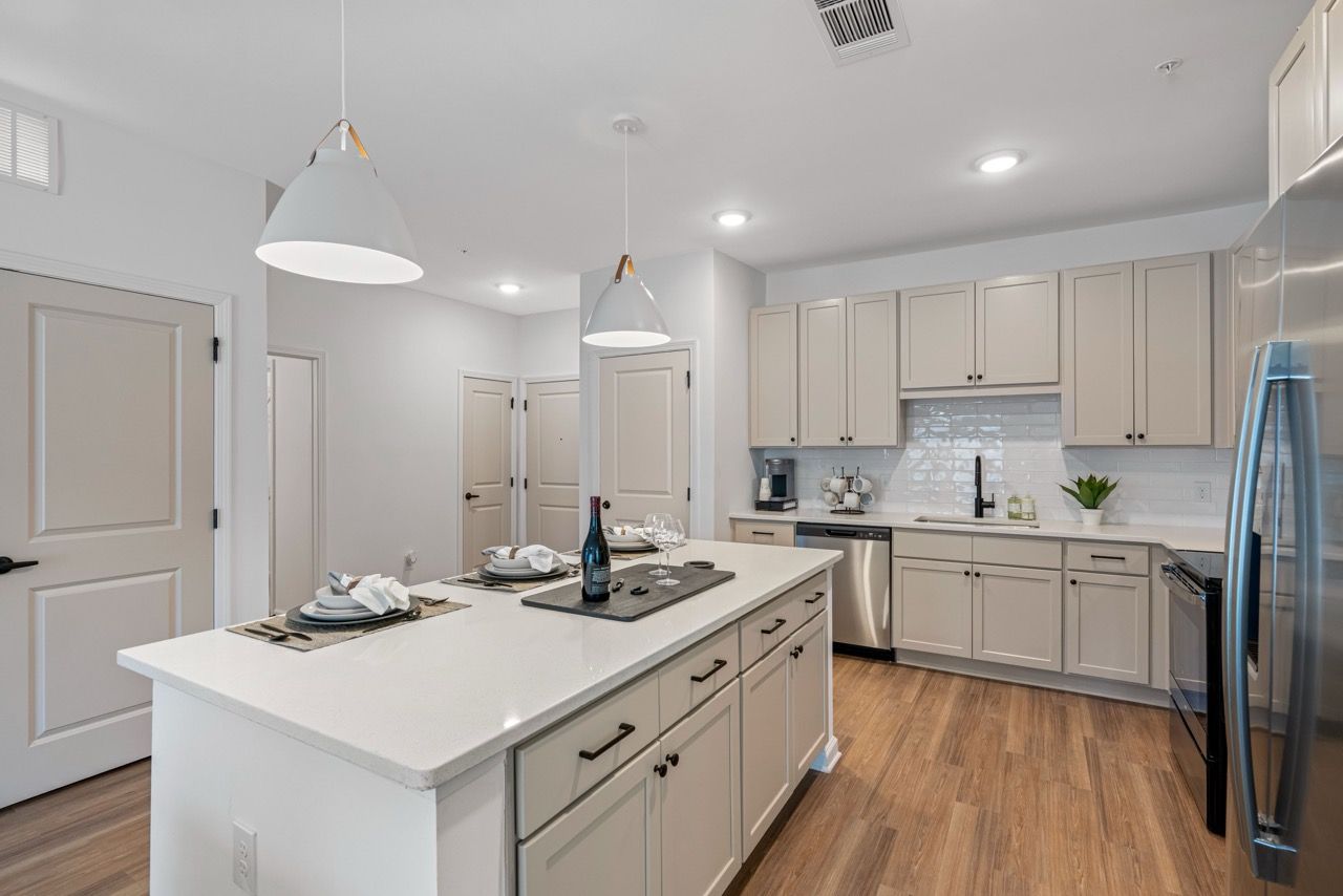 Modern kitchen in a neutral-toned apartment with an island, stainless steel appliances, and pendant lights.