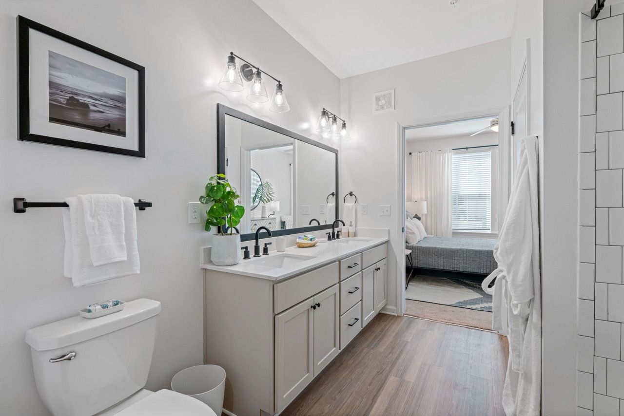 Modern bathroom with double-sink vanity, large mirror, and doorway to the bedroom.