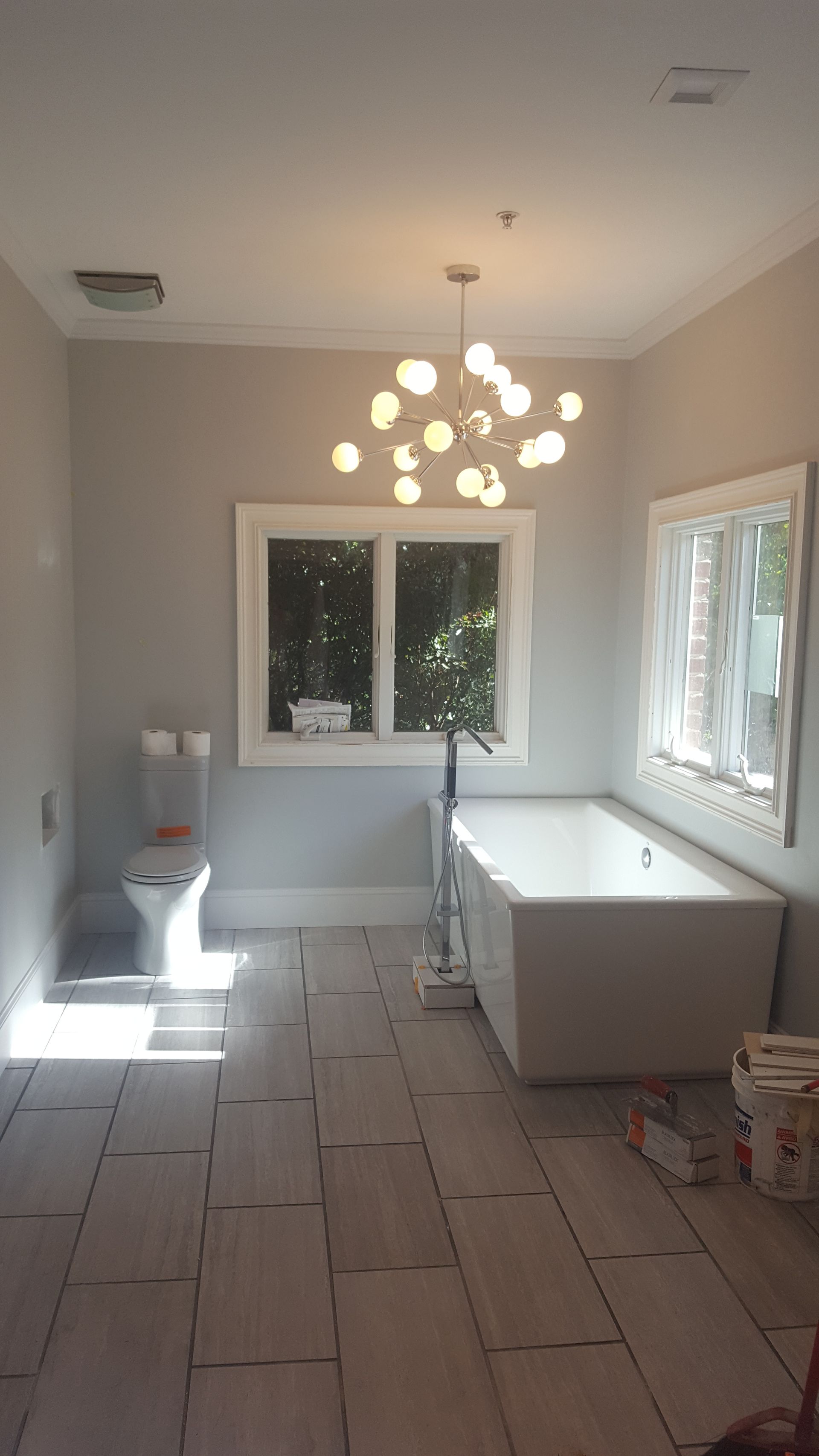 Bright kitchen under renovation with white cabinets, tiled floor, and a hanging chandelier