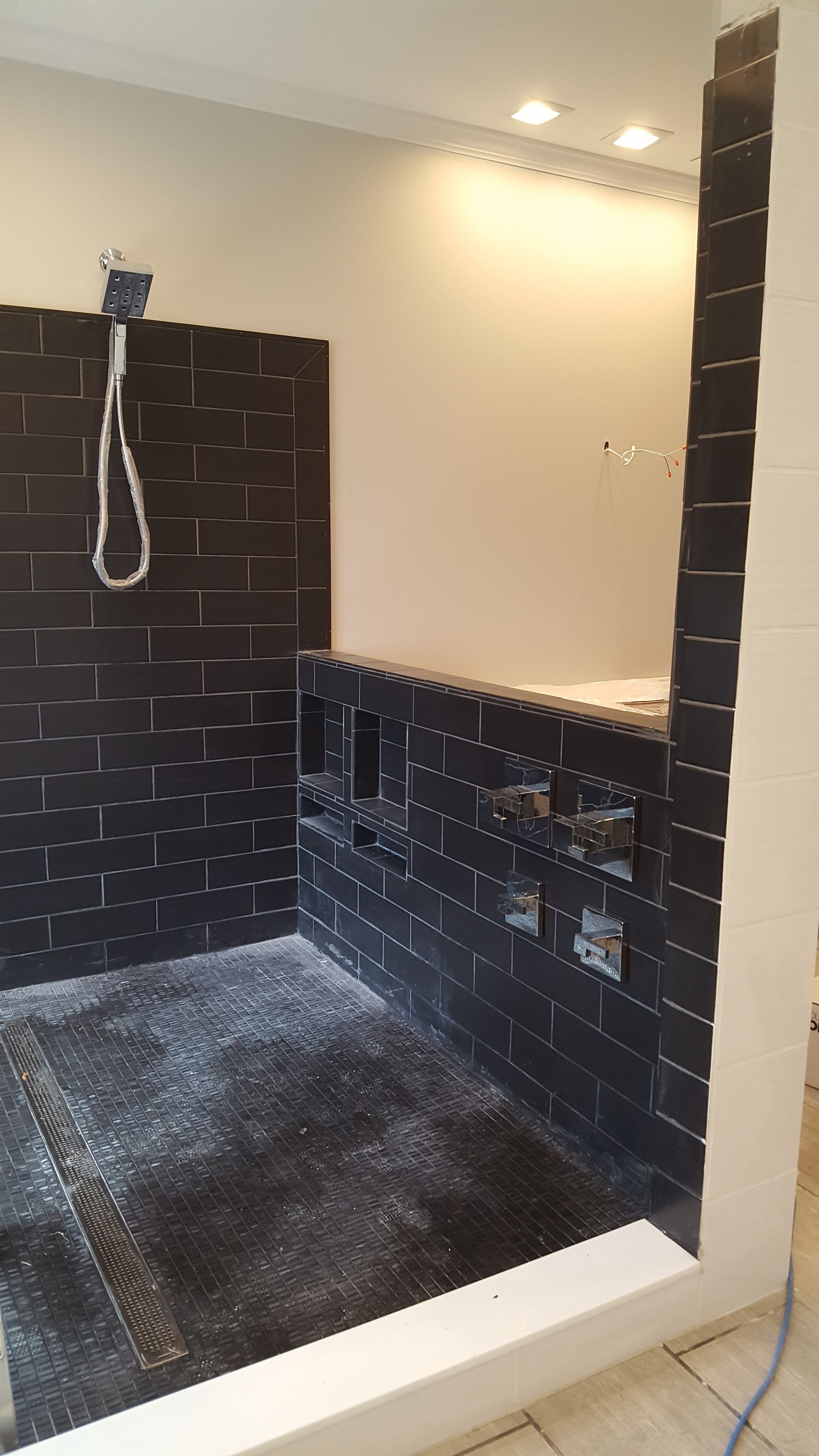 Black-tiled shower under construction with white bench, showerhead pipe, and unfinished floor.