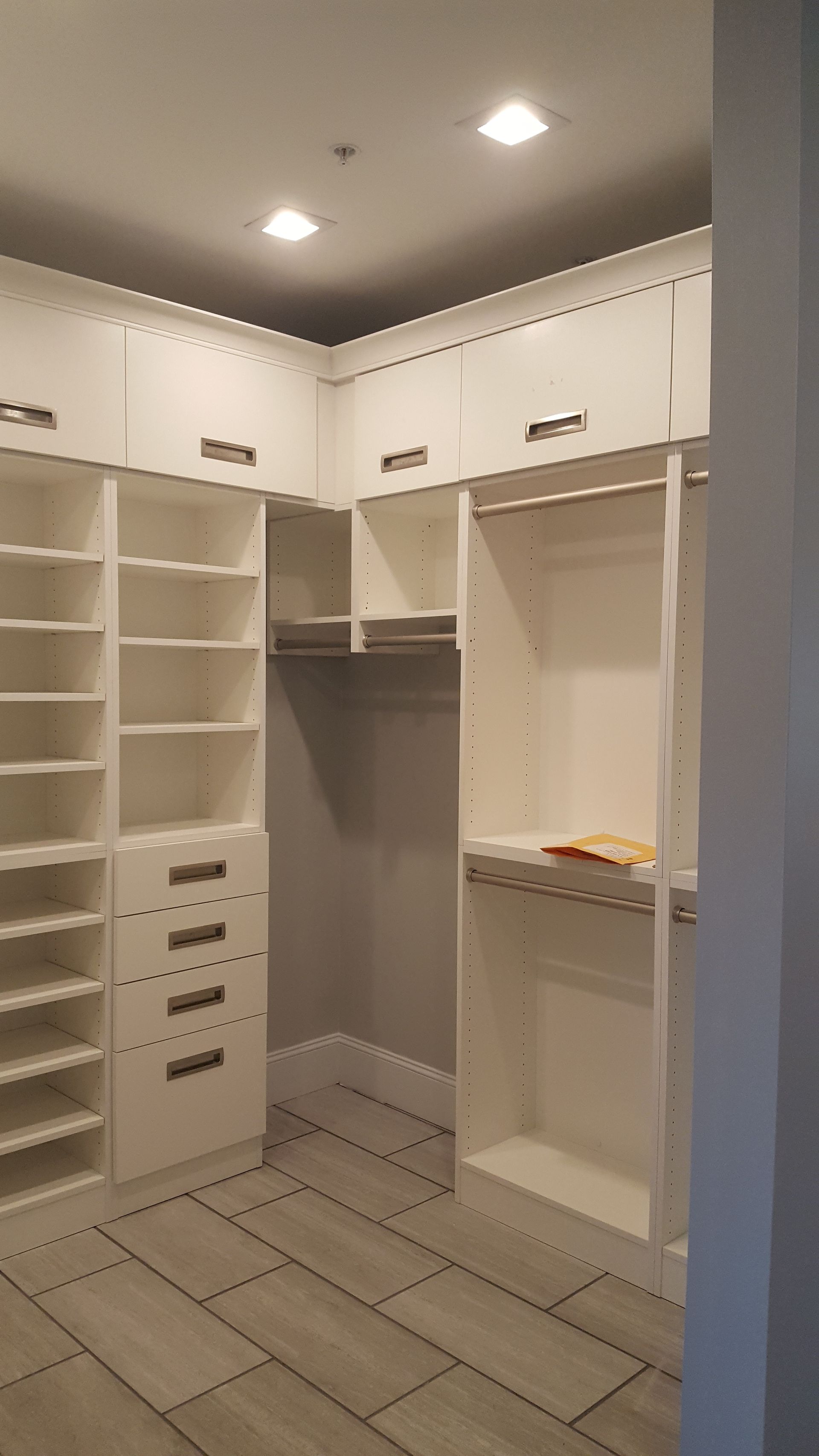 White walk-in closet with shelves, drawers, hanging rods, and tiled floor under ceiling lights