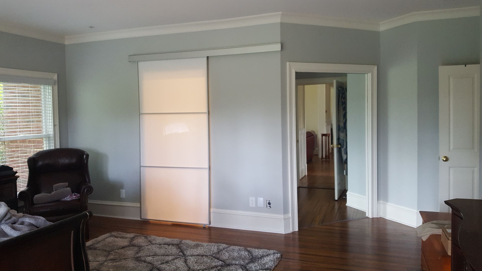 Living room with pale blue walls, hardwood floor, white closet doors, and a black chair by the window.