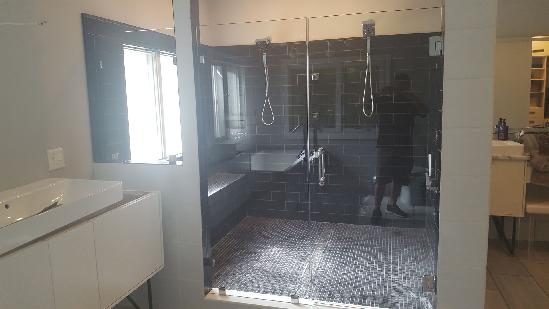 Modern bathroom with glass shower enclosure, dark tile, and white vanity sink