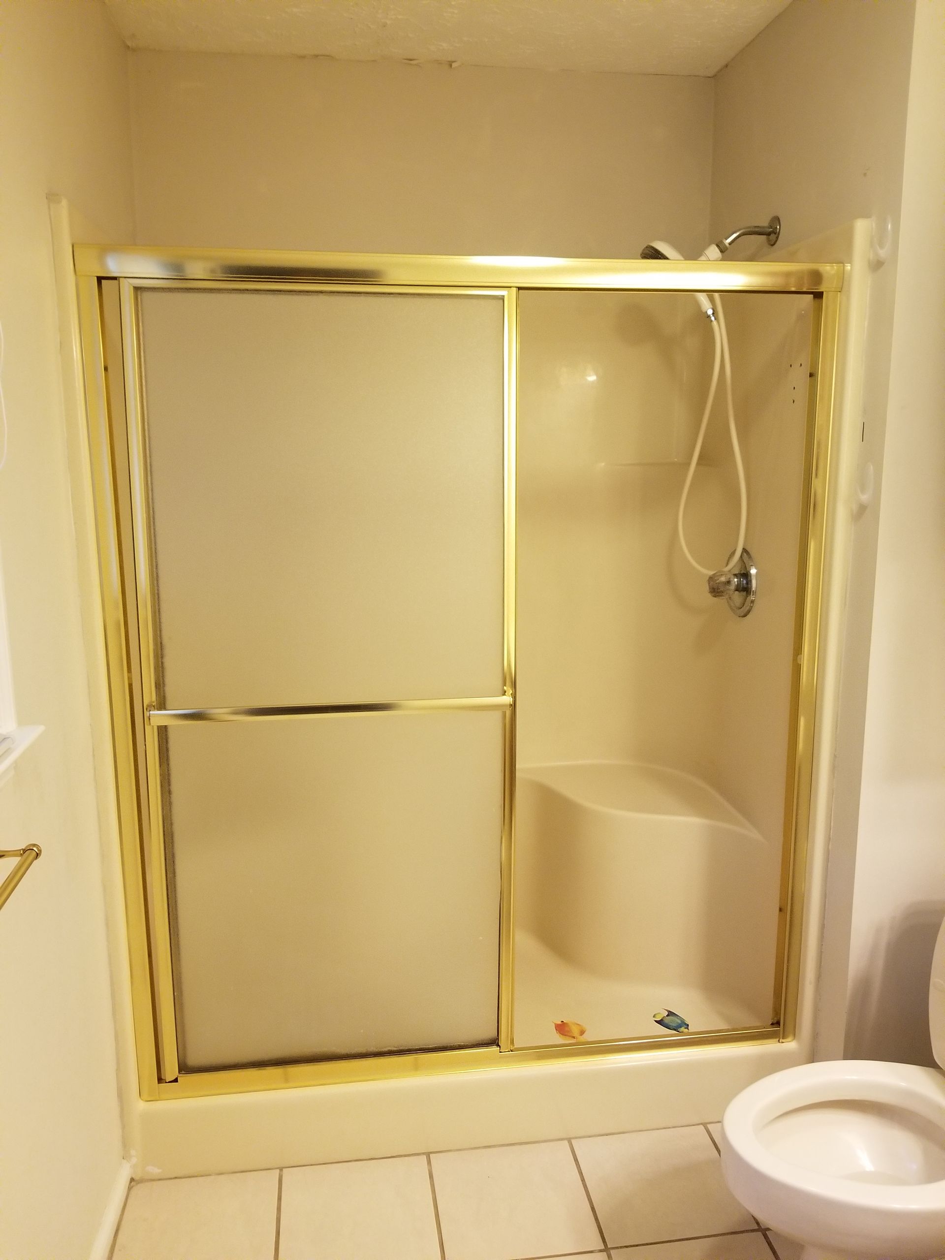 Bathroom shower with gold-framed sliding glass doors and a showerhead inside.