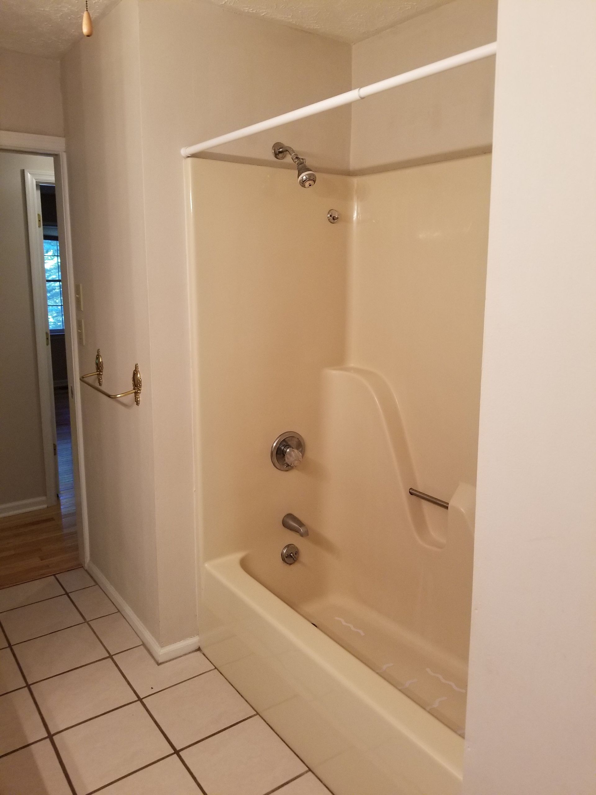 Bathroom with a beige shower-tub combo, white tile floor, and a towel bar on the wall.