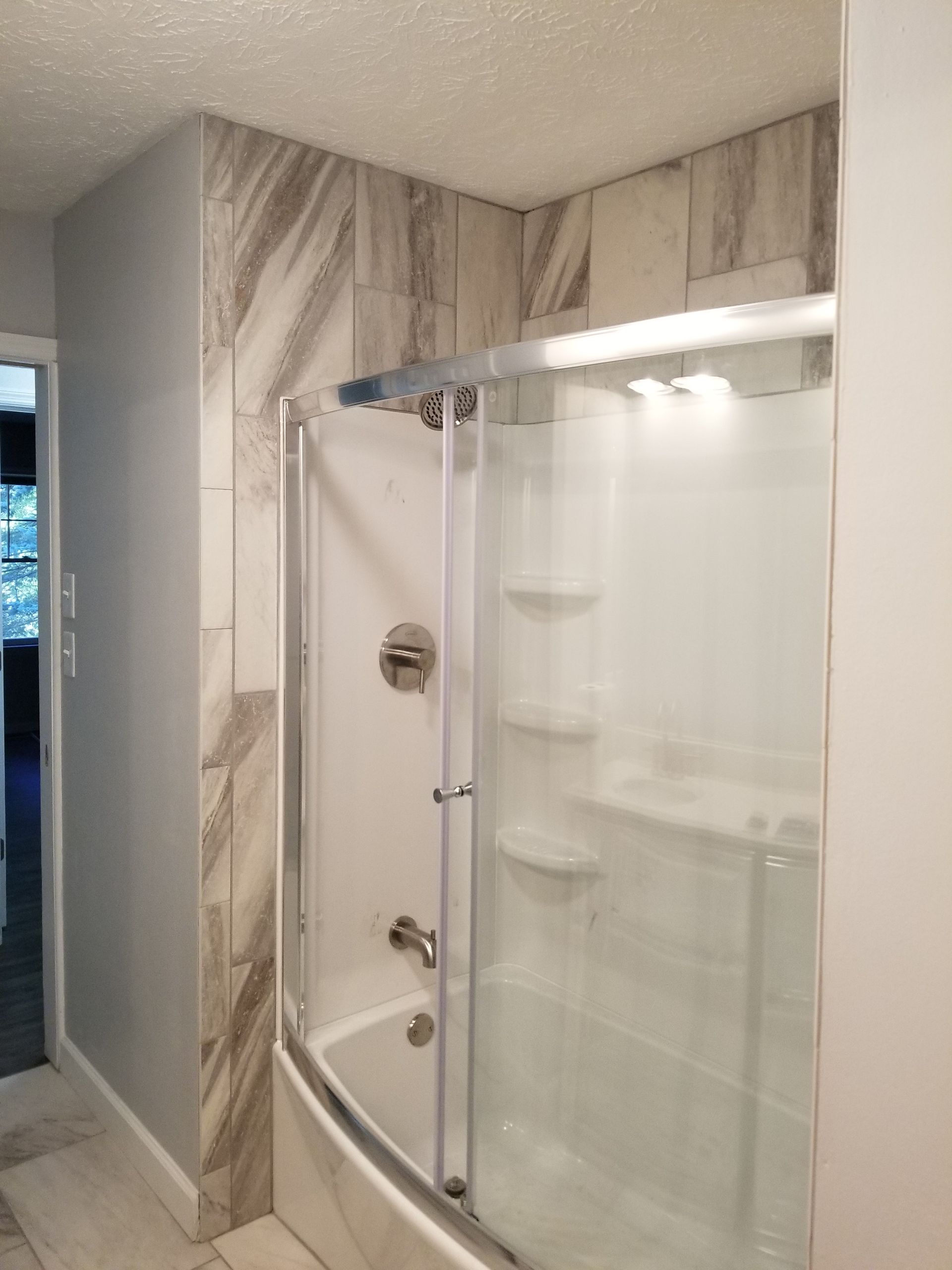 Compact shower stall with sliding glass doors and marble-pattern tile walls