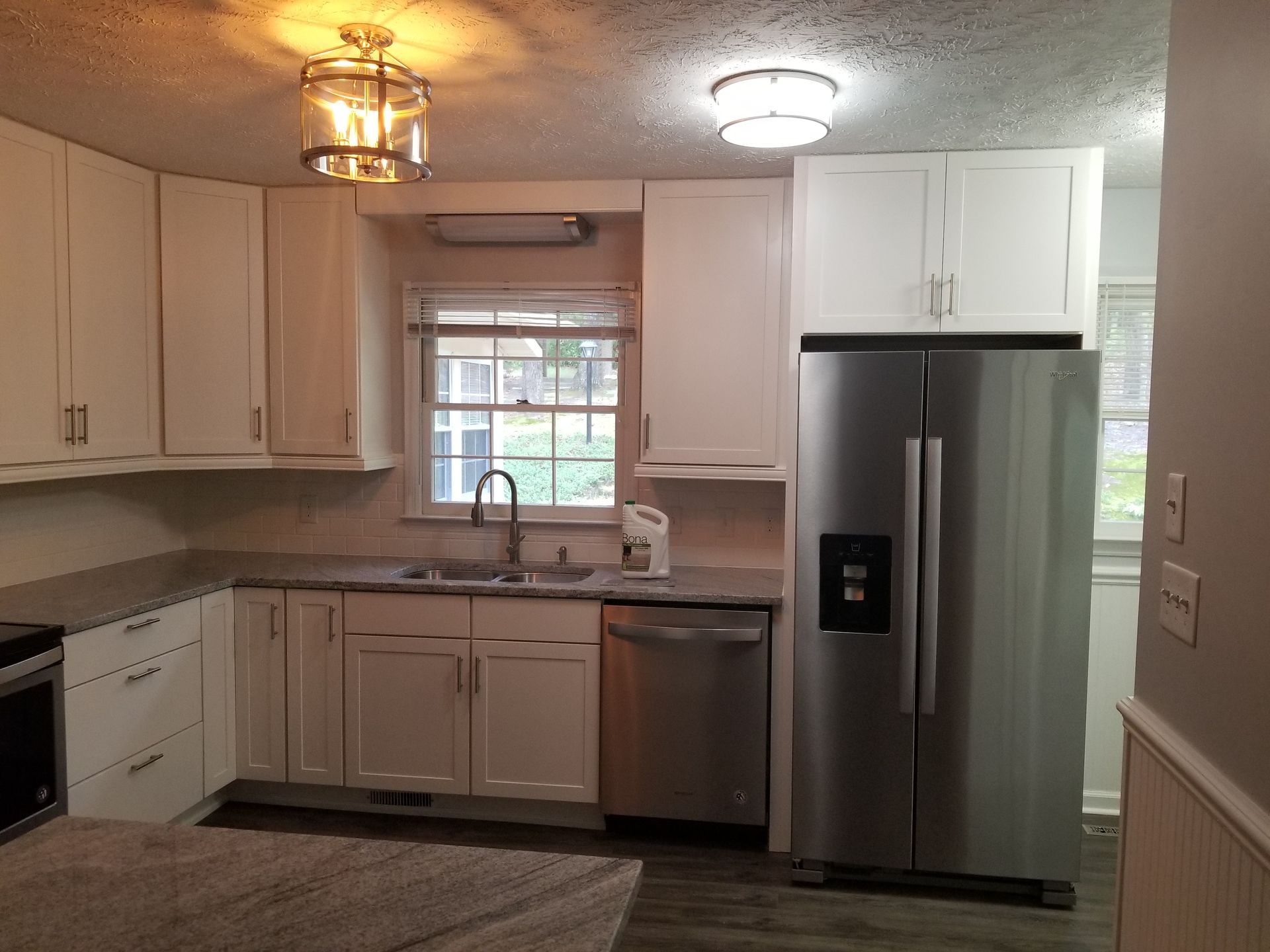 Kitchen interior with white cabinets, stainless steel fridge, and a window over the sink.