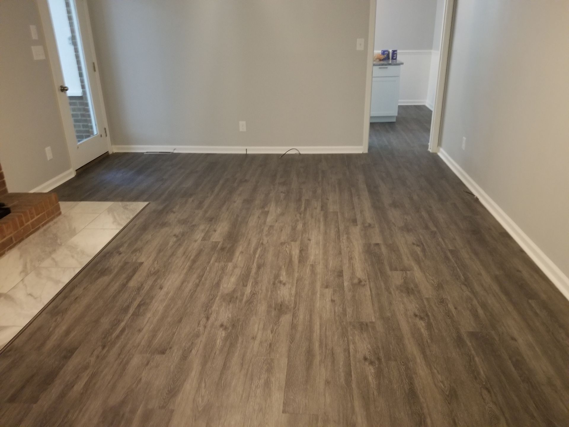 Empty living room with gray walls, wood-look flooring, and a view into a kitchen area