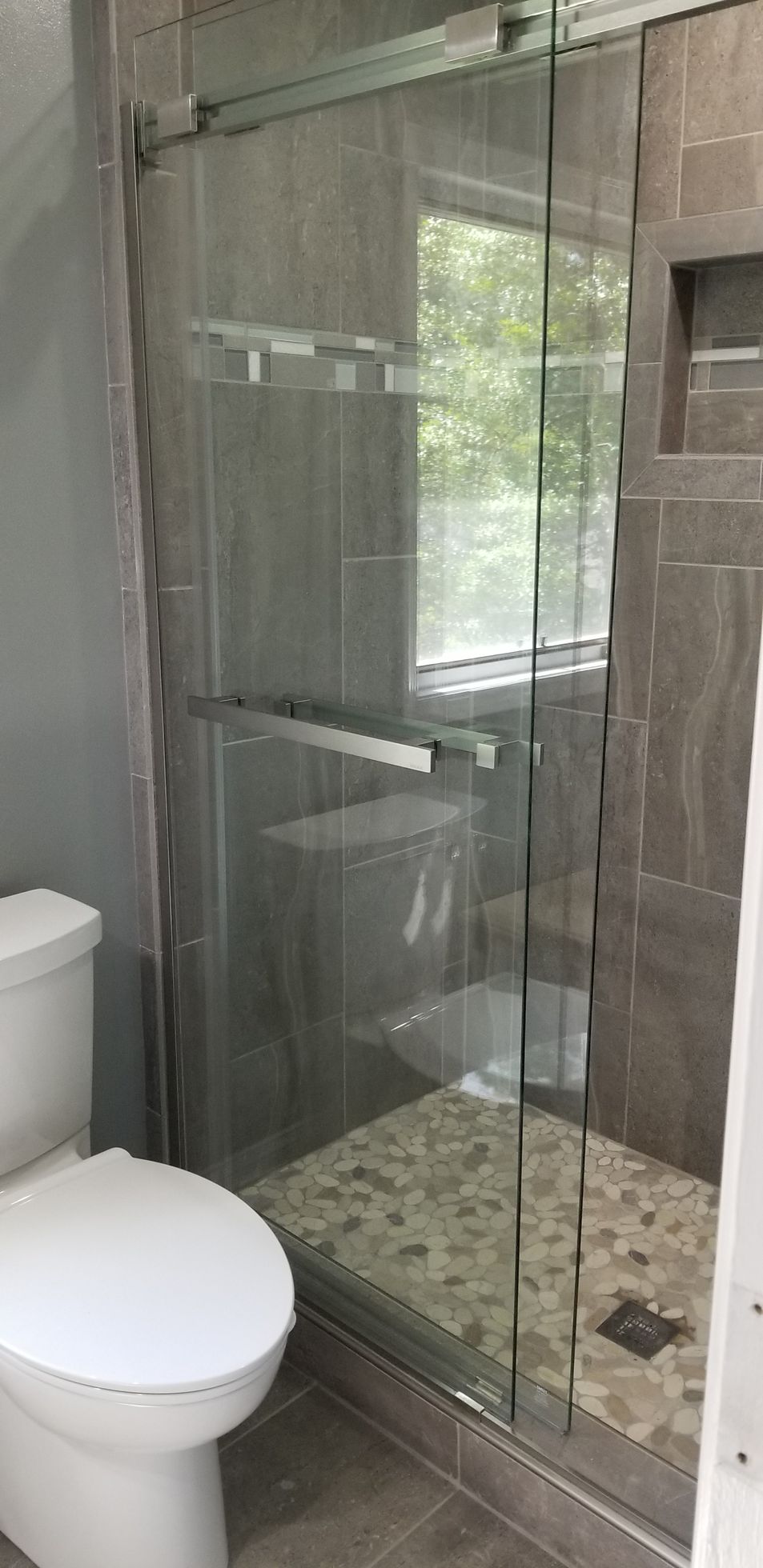Bathroom with glass walk-in shower, gray tile, and a toilet in the foreground.