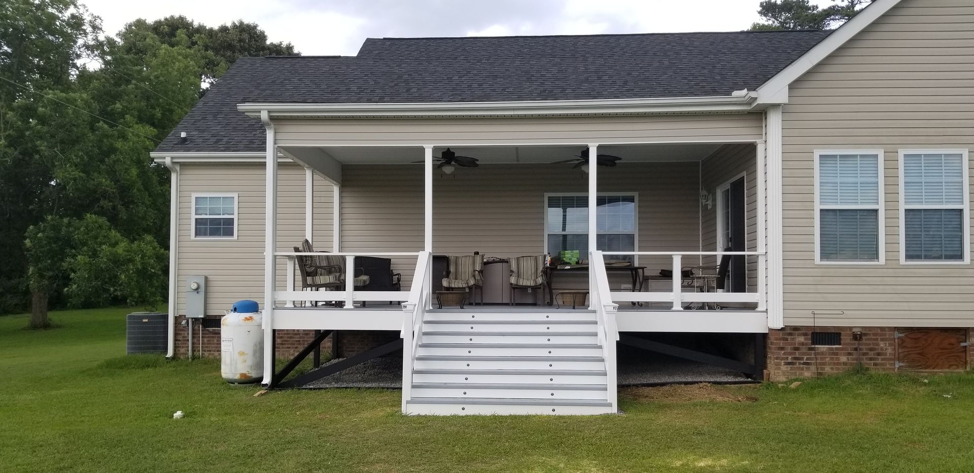 Front porch with white railing and steps on a beige house, with patio furniture and a lawn in front.