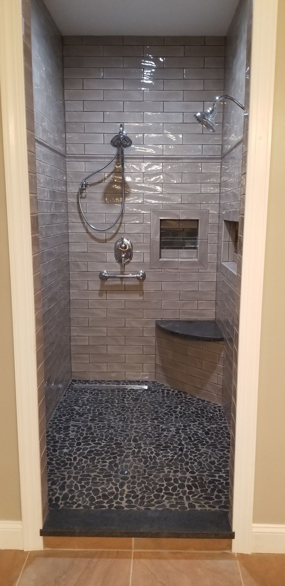 Bathroom shower with beige tile, glass door, wall-mounted fixtures, and a built-in bench seat.